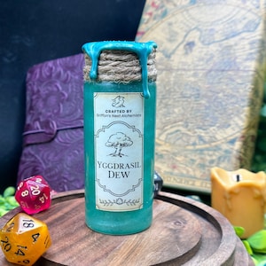 May include: A teal-colored potion bottle with a label that reads "Yggdrasil Dew." The bottle is sealed with a teal wax and twine. The label also says "Crafted by Griffon's Nest Alchemists." The bottle sits on a wooden stand with dice in the background.