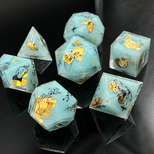 May include: Set of six blue and gold dice with a hand and moon design. The dice are made of resin and have a matte finish.
