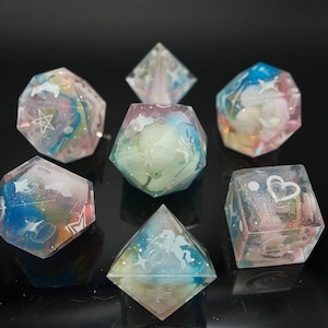 May include: Set of seven iridescent dice with white glitter and white designs. The dice are clear and have a variety of shapes, including a d4, d6, d8, d10, d12, and d20.