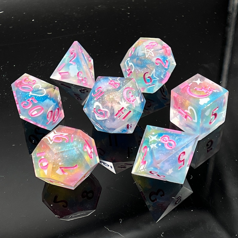 May include: Set of seven iridescent dice with pink and white swirls and pink numbers. The dice are translucent and have a glittery finish.