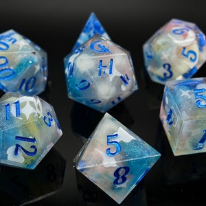 May include: A set of seven polyhedral dice with a cloudy, translucent blue and white swirl pattern. The dice have blue numbers and a white star design.