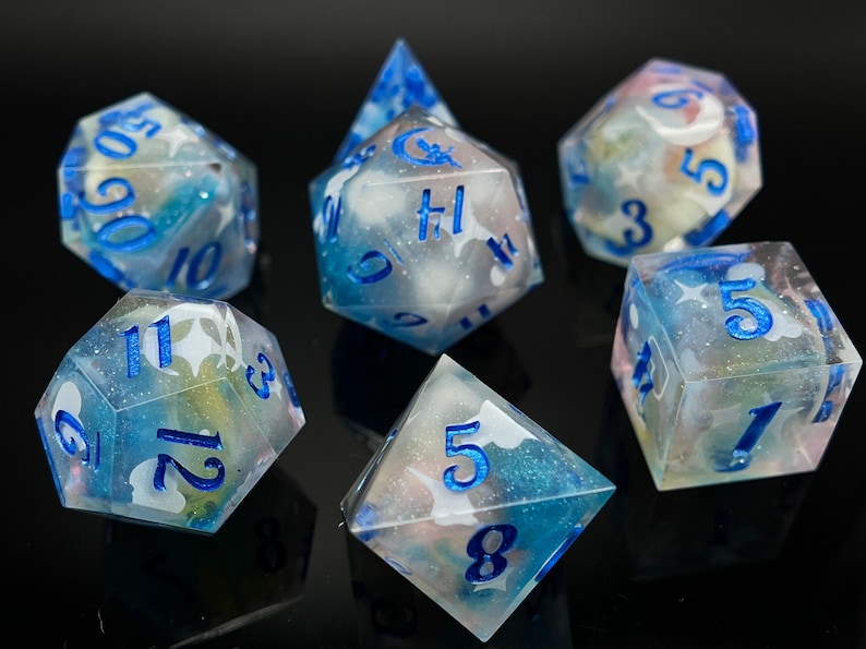 May include: A set of seven polyhedral dice with a cloudy, translucent blue and white swirl pattern. The dice have blue numbers and a white star design.