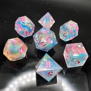 May include: Set of seven iridescent dice with pink numbers and symbols. The dice are translucent and have a cloudy, galaxy-like appearance. The dice are ideal for tabletop role-playing games.