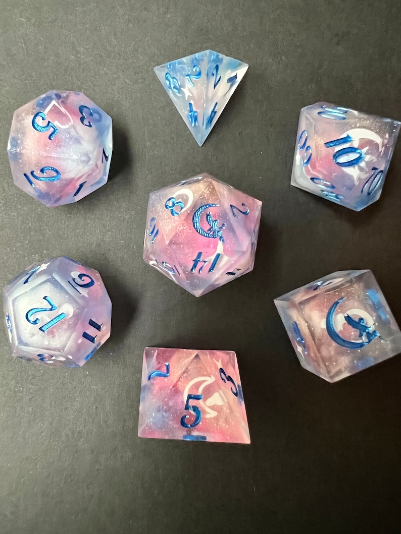 May include: Set of seven iridescent dice with a galaxy-like swirl pattern and blue accents. The dice are numbered 1-6, 1-10, 1-12, 1-20, 1-30, 1-100, and 1-6. The dice are made of clear resin with a galaxy-like swirl pattern and blue accents.