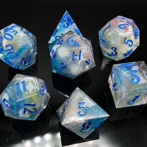 May include: Set of seven iridescent dice with blue and white swirls and blue numbers. The dice are shaped like a variety of polyhedrons, including a d4, d6, d8, d10, d%, d12, and d20.