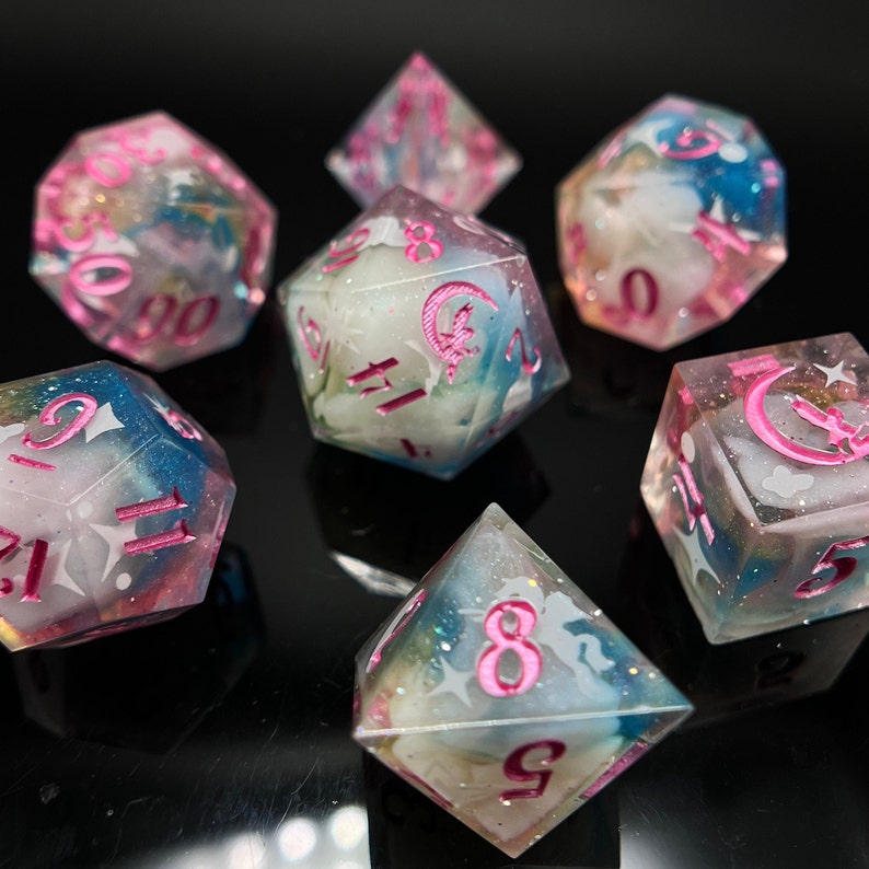 May include: Set of six iridescent dice with pink and white swirls and pink numbers. The dice are made of clear resin and have a cloudy, translucent appearance.