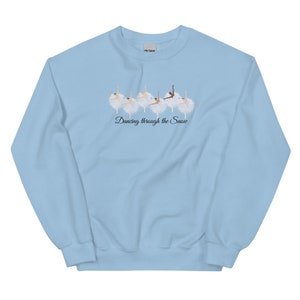 May include: Light blue sweatshirt with a graphic of ballerinas dancing in the snow. The text "Dancing through the Snow" is printed below the ballerinas.