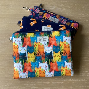 May include: Three zipped pouches with vibrant patterns. The top pouch features a navy blue background with an elephant and floral design. The middle pouch is navy blue with a fox pattern. The bottom pouch has a cat pattern with the text "Fluffy Bee".
