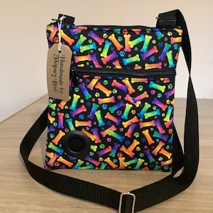 May include: A black crossbody bag with a rainbow bone and paw print design. The bag has a zippered closure and a black strap. The tag on the bag reads "Handmade by Hopsey Boo".