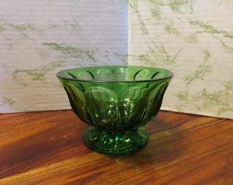 May include: A green glass bowl with a fluted design and a pedestal base. The bowl is made of clear glass with a green tint.
