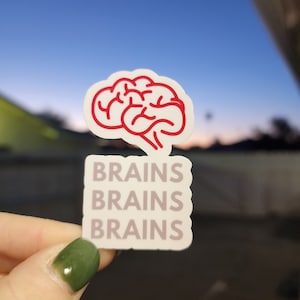 Puede incluir: Una pegatina blanca con un contorno rojo de un cerebro y la palabra "BRAINS" repetida tres veces.