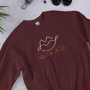 May include: A maroon sweatshirt with a white outline of a pair of lips and the text "Puh Tuck Kuh" in orange.