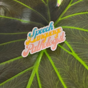 Puede incluir: Una pegatina blanca con el texto "Speech Language Pathologist" en una fuente retro. El texto está en diferentes colores, incluyendo azul, amarillo y rosa.