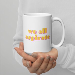 May include: White ceramic mug with a yellow and pink graphic that says "we all aspirate".