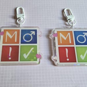 Pode incluir: Dois chaveiros quadrados com fecho de metal branco. Cada chaveiro tem um design colorido com as letras "MO", um s&iacute;mbolo masculino, um ponto de exclama&ccedil;&atilde;o e uma marca de verifica&ccedil;&atilde;o. Acentos de cora&ccedil;&atilde;o rosa nos cantos.