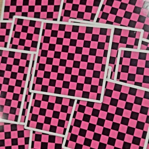 May include: A collection of square stickers featuring a repeating black and hot pink checkered pattern. Each individual sticker has a thin white border surrounding the vibrant, high-contrast grid design, layered together in a scattered pile.