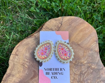 Puede incluir: Un par de pendientes de forma de lágrima hechos con cuentas de color rosa iridiscente y doradas. Los pendientes están sobre una tarjeta blanca con el texto "Northern Beading Co."