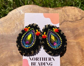 May include: A pair of black beaded earrings with iridescent teardrop-shaped stones and colorful accents. The earrings are on a white card with the text "NORTHERN BEADING CO."