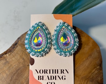 May include: Teal and white beaded earrings with iridescent teardrop-shaped crystals. The earrings are on a card that says "Northern Beading Co."
