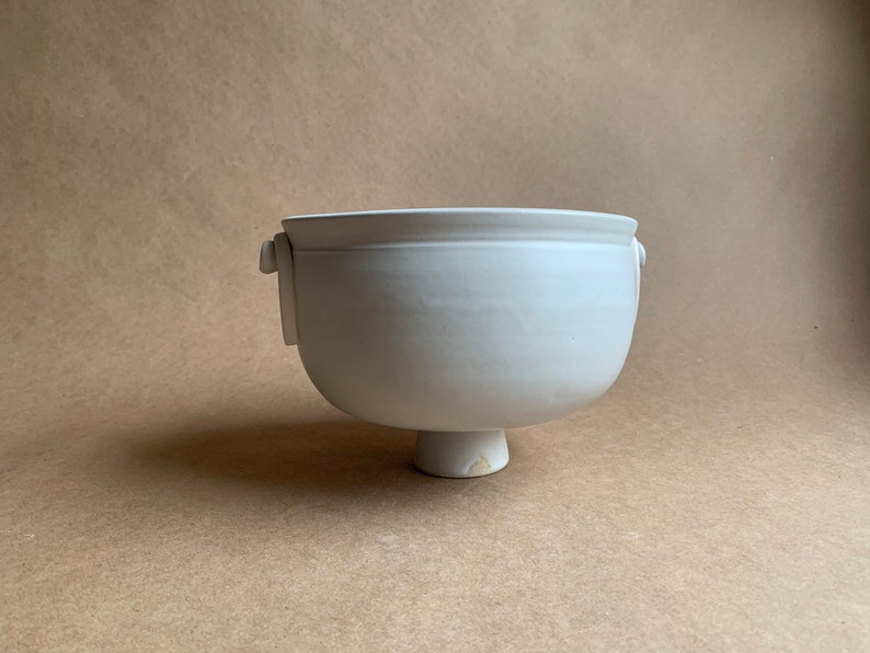 May include: White ceramic bowl with two handles and a pedestal base.