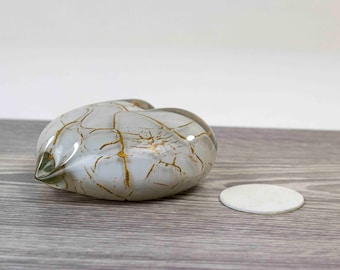 Pode incluir: Um vaso de vidro branco em forma de coração com detalhes de craquelado dourado. O vaso está sobre uma superfície de madeira.