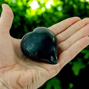 May include: A dark green heart-shaped stone held in an open hand.