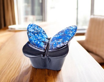 May include: A blue and white butterfly-shaped ceramic figurine with a glossy finish. The figurine is sitting on a wooden table.