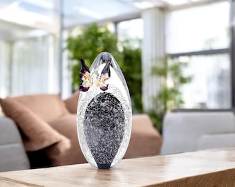 May include: A clear glass vase with a black and white speckled interior. A pair of purple and yellow butterflies are attached to the outside of the vase.