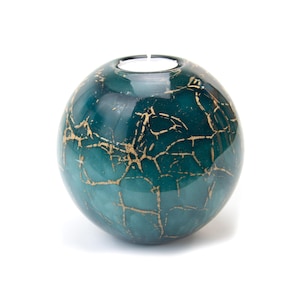 Op de afbeelding: Een teal-kleurige, bolvormige kandelaar met een gouden craquelé-patroon. De bovenkant heeft een cirkelvormige opening voor een waxinelichtje. Het decoratieve glazen stuk is een uniek woondecoratie-item.