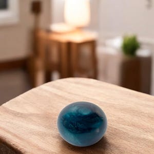 May include: A dark blue glass sphere with swirling patterns sits on a wooden surface.