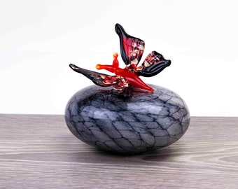 May include: A red and black glass butterfly figurine perched on a gray, marbled, glass rock.