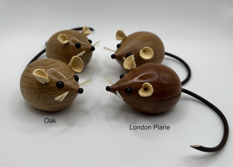 Puede incluir: Cuatro figuras de rat&oacute;n de madera con cuerpos lisos y redondeados, ojos de cuentas negras y bigotes finos y claros. Dos ratones est&aacute;n etiquetados como Oak, mostrando una veta de madera clara, y dos como London Plane, con un acabado pulido oscuro.