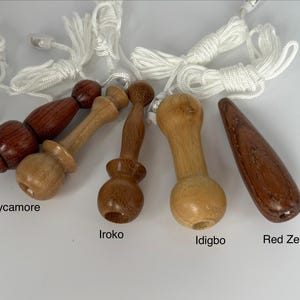 Può includere: Cinque tiranti per tende in legno di varie forme e tipi di legno, etichettati Bubinga, Sycamore, Iroko, Idigbo e Red Zebrano. Ogni tirante presenta una finitura tornita liscia ed è fissato a un cordino di nylon bianco con un piccolo fermo in plastica.
