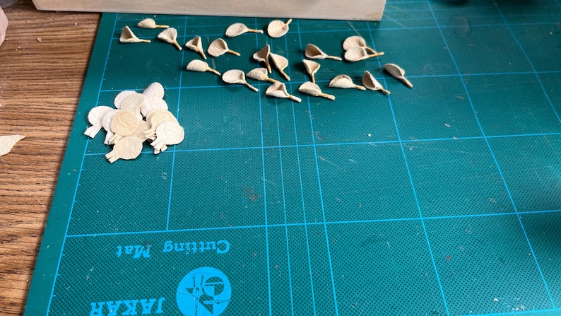 Puede incluir: Una colecci&oacute;n de peque&ntilde;as formas de papel troquelado de color beige claro que se asemejan a p&eacute;talos de flores u hojas. Algunas piezas est&aacute;n dispuestas en un grupo suelto a la izquierda, mientras que otras est&aacute;n esparcidas individualmente.