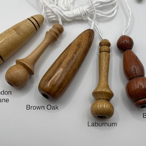 Op de afbeelding: Vijf houten lichtknoppen met witte koorden, gelabeld Iroko, London Plane, Brown Oak, Laburnum en Bubinga. Elke knop heeft een unieke gedraaide vorm en houtnerf, variërend van lichtbruin tot diepe roodbruine tinten, gerangschikt in een rij.
