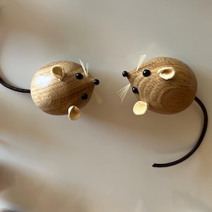 Puede incluir: Varias figuras peque&ntilde;as de ratones de madera redondeadas dispuestas en un patr&oacute;n. Cada rat&oacute;n presenta un cuerpo de madera de color marr&oacute;n claro con vetas, dos orejas peque&ntilde;as redondeadas, ojos de cuentas negras, un hocico puntiagudo con bigotes blancos finos y una cola larga, fina y oscura.