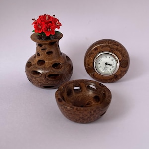 May include: A wooden decorative set featuring a vase with red flowers, a small bowl, and a round clock. The objects are made of brown wood with a unique, porous design. The clock has a white face with black numbers and hands.