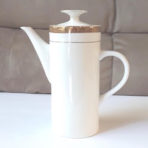 May include: A white porcelain coffee pot with a gold rim and lid. The pot has a long spout and a curved handle. The design is simple and elegant, suitable for serving coffee or tea. The pot is approximately 10 inches tall.