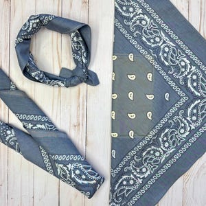 May include: Two gray paisley bandanas with white and black designs. One bandana is folded into a triangle shape and the other is folded into a circle.
