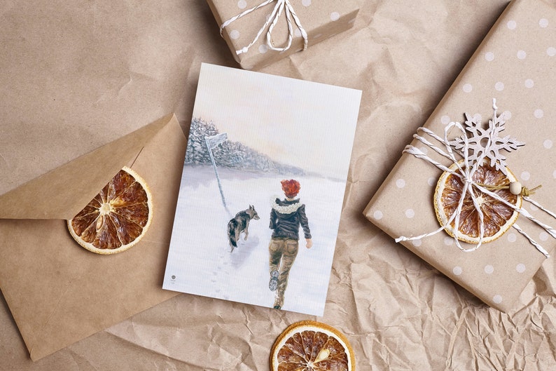 Op de afbeelding: Een aquarel schilderij van een persoon en een hond die door een besneeuwd bos lopen. De persoon draagt een rode hoed en een bruin jack. De hond is bruin en wit.