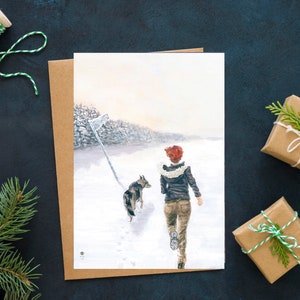 Op de afbeelding: Een aquarel van een vrouw en een hond die door een besneeuwd bos rennen. De vrouw draagt een rode hoed en een bruin jack. De hond is een grijs-witte wolfshond.