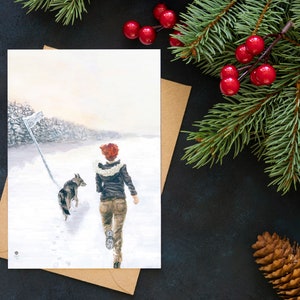 Op de afbeelding: Een aquarel schilderij van een vrouw en een hond die door een besneeuwd bos lopen. De vrouw draagt een bruin jack en een spijkerbroek, en de hond is een grijs-witte husky.