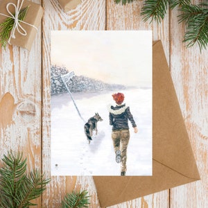 Op de afbeelding: Een vrouw in een bruin jack en jeans loopt door een besneeuwd landschap met een hond. De vrouw draagt een rode sjaal en de hond is bruin en wit.