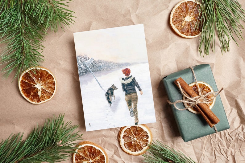 Op de afbeelding: Een kaart met een schilderij van een vrouw en een hond die door een besneeuwd bos lopen. De vrouw draagt een rode hoed en een bruin jack. De hond is een bruin-witte Duitse herder.
