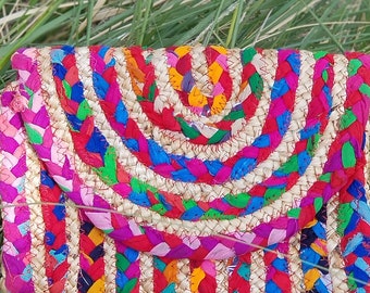 May include: A colorful woven clutch purse with a rainbow pattern. The clutch is made of straw and has a unique design with a curved top.