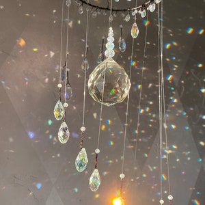 May include: A decorative crystal chandelier with a circular frame and multiple strands of clear crystals. The crystals are various shapes, including teardrops and spheres. The light refracts through the crystals, creating a rainbow effect.