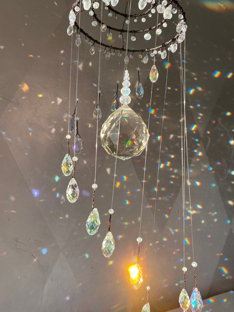 May include: A decorative crystal chandelier with a circular frame and multiple strands of clear crystals. The crystals are various shapes, including teardrops and spheres. The light refracts through the crystals, creating a rainbow effect.