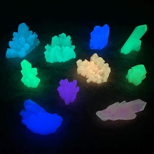 May include: A collection of glowing crystal formations in various colors, including blue, green, purple, and white, against a dark background. The crystals have a textured appearance and emit a soft, ethereal light, creating a mystical ambiance.