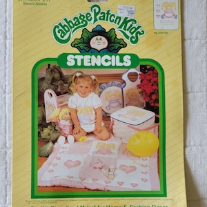 May include: A yellow Cabbage Patch Kids stencil package containing 4 pre-cut 8.5 inch by 11 inch Mylar stencil sheets. The packaging features a graphic of a child with a doll, a picnic basket, and a quilt decorated with heart patterns.