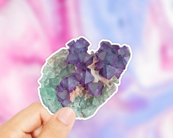 Könnte beinhalten: Ein Nahaufnahme eines violetten und grünen Kristall-Aufklebers. Der Kristall hat eine raue, natürliche Textur und ist eine beliebte Wahl für dekorative Zwecke.